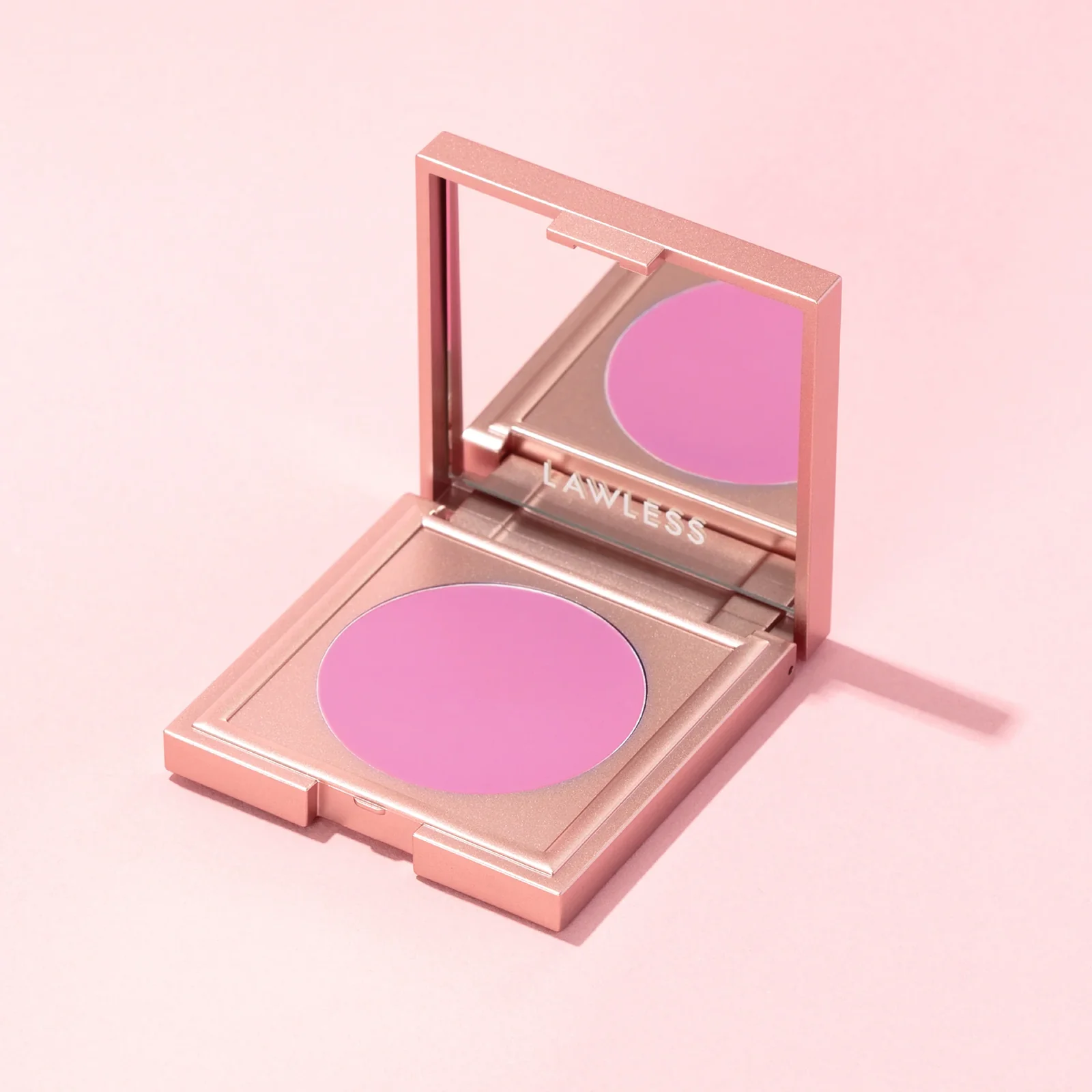 Open rose-gold blush compact with a pink pan on a soft pink background.